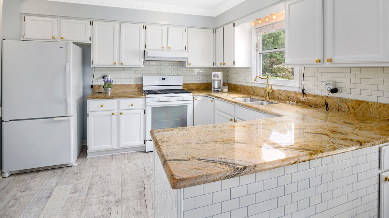 Bright kitchen featuring white kitchen cabinets with gold hardware and polished granite countertops. Bright kitchen featuring white kitchen cabinets with gold hardware and polished granite countertops.
