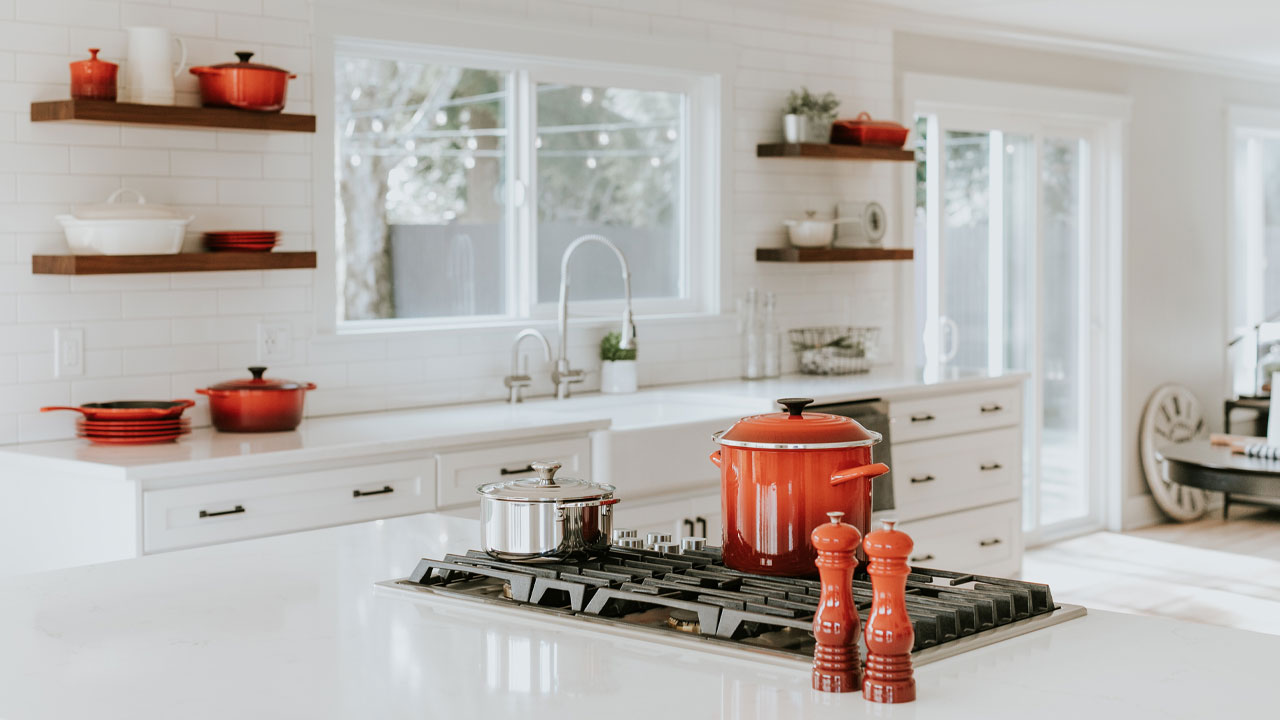 Modern kitchen featuring white kitchen cabinets with red dishware and cookware on open shelves and stovetop. Modern kitchen featuring white kitchen cabinets with red dishware and cookware on open shelves and stovetop.