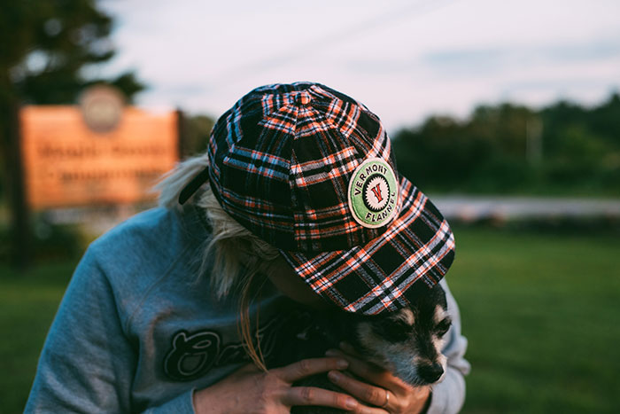 Person in a plaid cap cuddling a small dog outdoors, showcasing why dogs like to cuddle.
