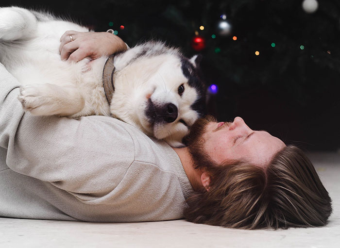 Man cuddling with a dog under a Christmas tree.