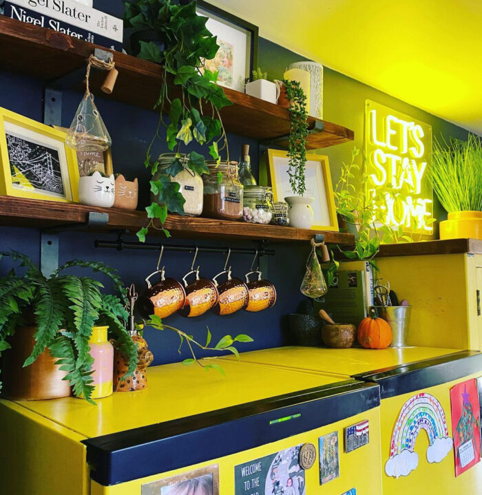 Shelves with kitchen items on the black wall near the yellow cabinets