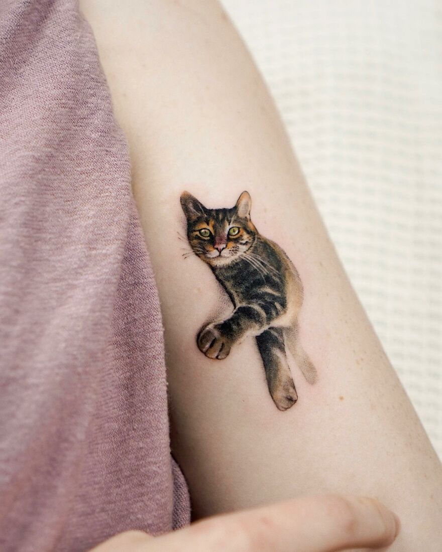 Tattoo of a cat on arm, showcasing painting-like style with nature elements by a Korean ink artist.