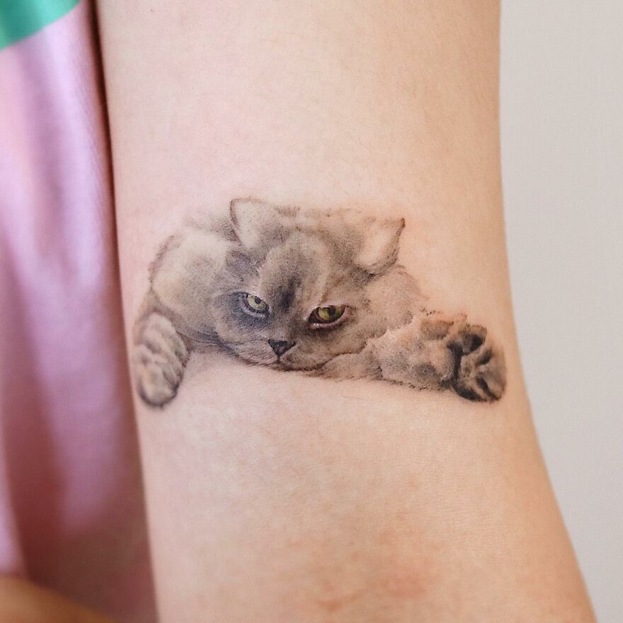 A painting-like tattoo of a gray cat with green eyes on a person's skin, showcasing nature and animal art.
