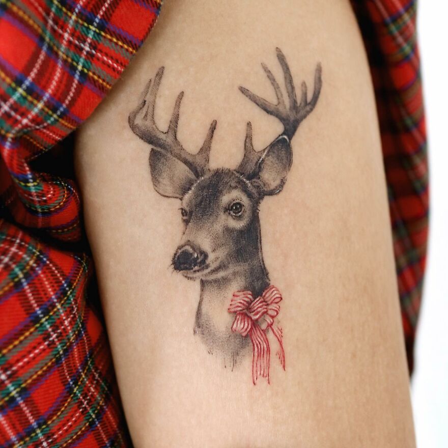 Tattoo of a deer with antlers and red bow, showcasing nature-inspired art by a Korean ink artist.