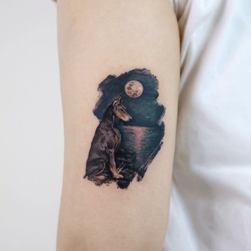 Tattoo of a dog by the ocean under a full moon, showcasing nature and animal elements in a painting-like style.