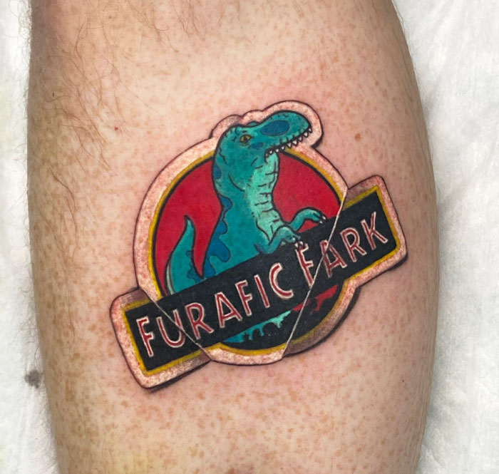 Cool dinosaur tattoo featuring a blue T-Rex with the words “Furafic Park” on a red background.