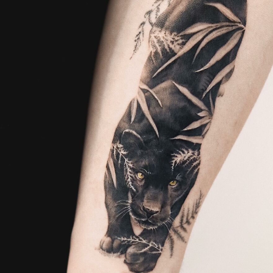 Tattoo of a black panther with nature elements on forearm, resembling a painting.