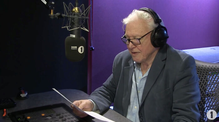 Elderly man wearing headphones and glasses in a radio studio, sharing positive stories that prove our world isn't a total nightmare.