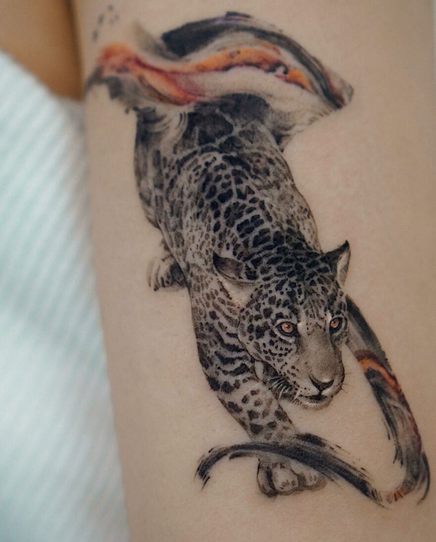 Tattoo of a leopard blending with nature elements on skin, featuring painting-like detail by Korean ink artist.