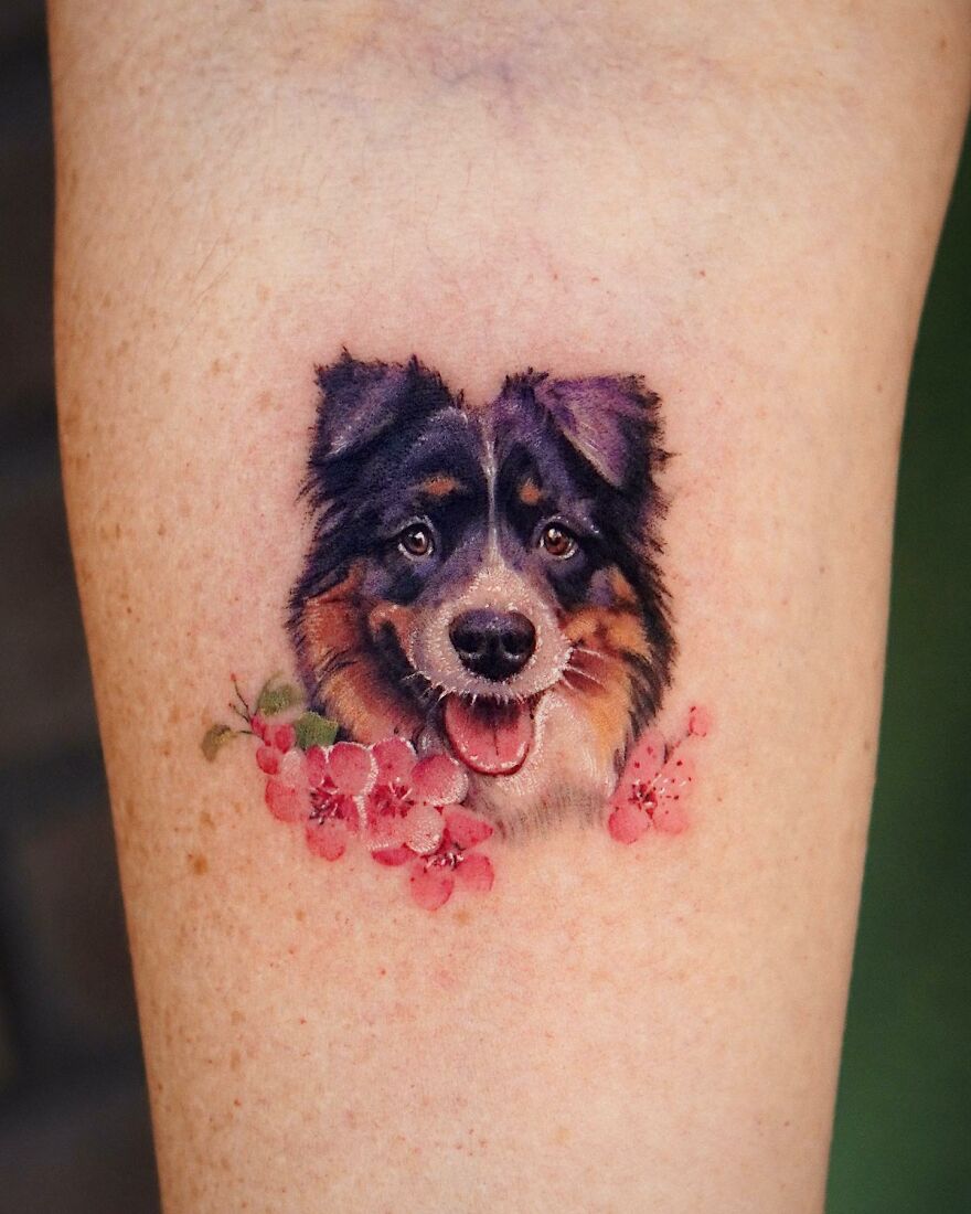 Tattoo of a dog's face with pink flowers, showcasing painting-like style by Korean ink artist.