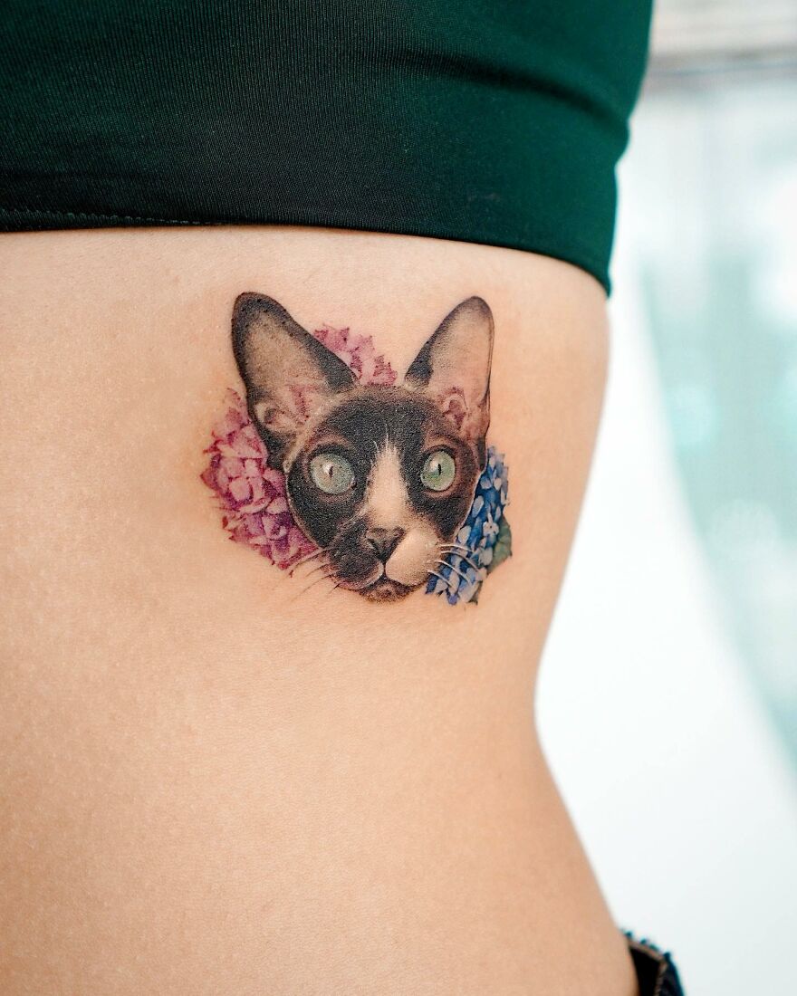 Tattoo of a cat surrounded by flowers, showcasing a nature-themed painting by a Korean ink artist.