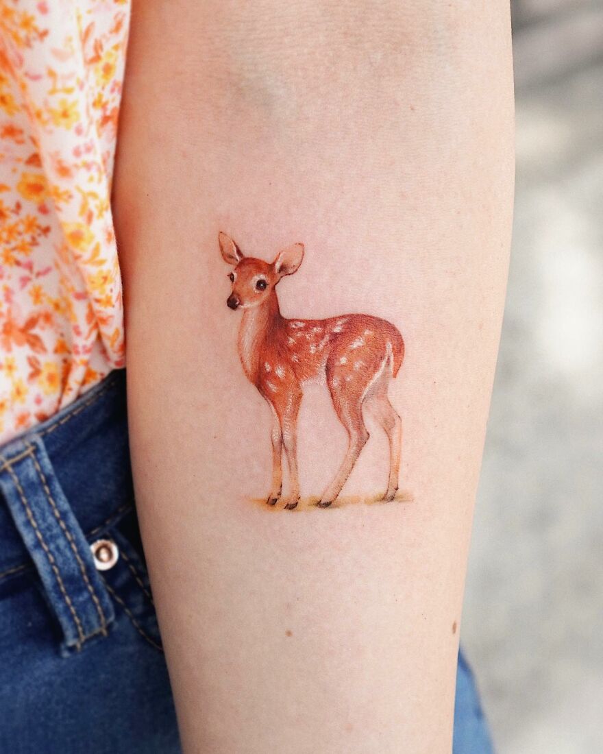Tattoo of a realistic fawn on forearm, showcasing painting-like artistry with nature elements.