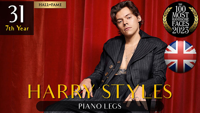 Man in a pinstripe suit seated against a red curtain, part of 2023's most handsome men ranking by The Independent Critics.