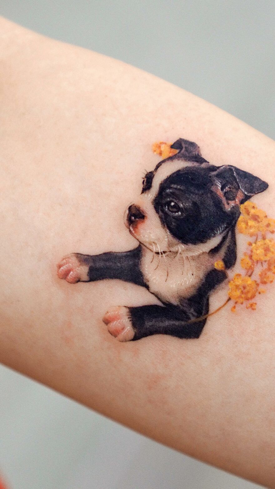 Tattoo of a black and white dog with yellow flowers, showcasing painting-like elements by a Korean ink artist.