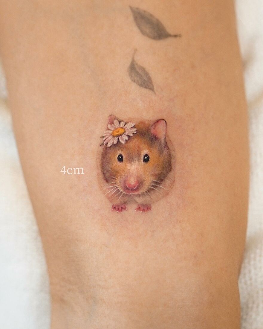 Tattoo of a small hamster with a daisy on its head, showcasing painting-like nature elements.
