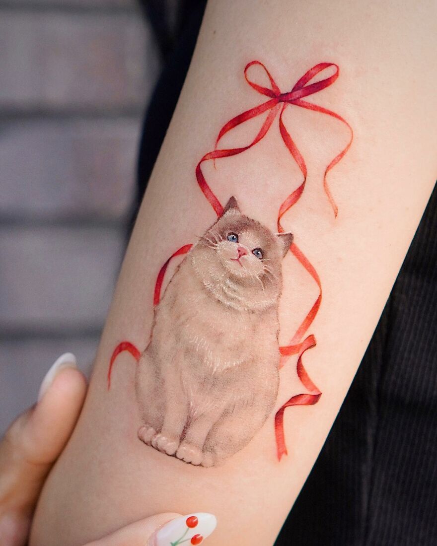Tattoo of a fluffy cat with a red ribbon, showcasing nature-inspired artistry.