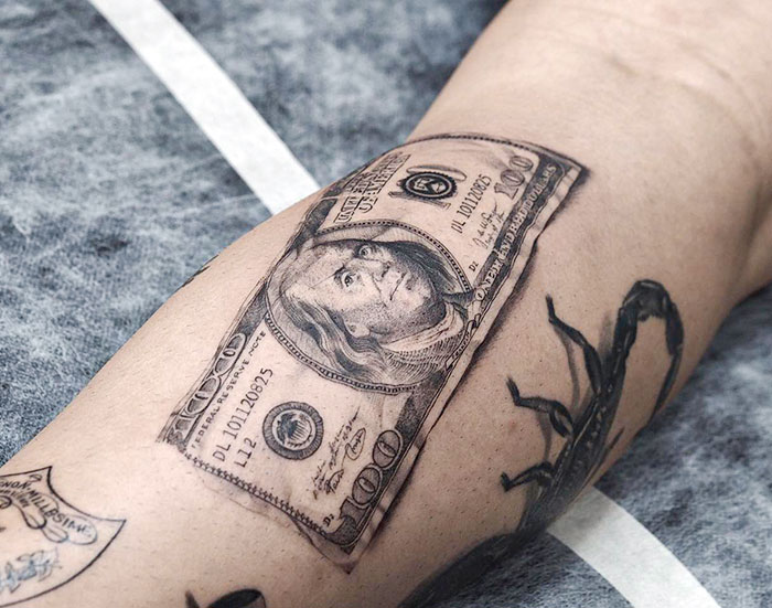 3D tattoo of a realistic $100 bill on a person's arm, showcasing impressive artistry and detail.