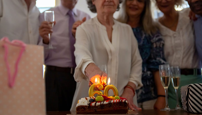 Elderly woman celebrating birthday with friends, cutting cake; longevity concept.