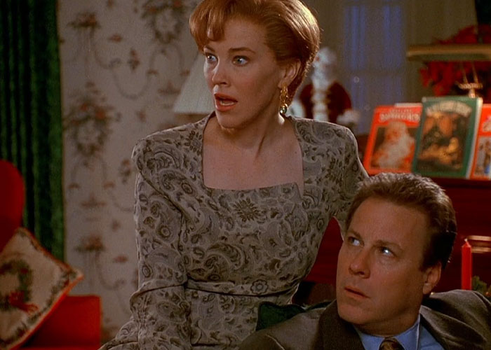 Catherine O'Hara as Kevin's mom in "Home Alone," wearing a 90s dress, looks surprised in a festive room.