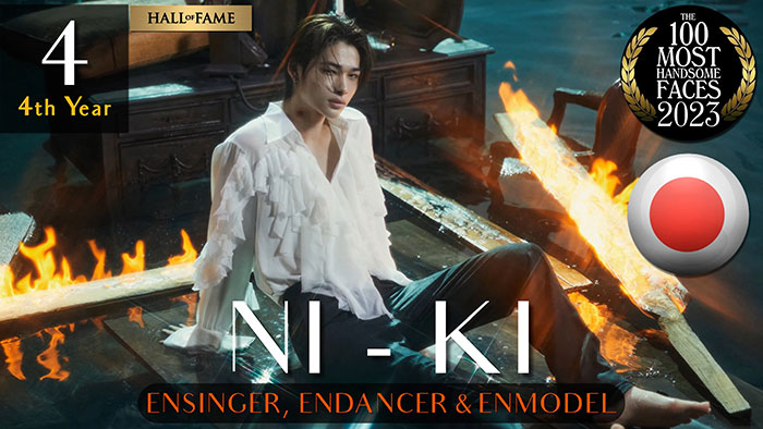 Handsome man ranked in 2023 by The Independent Critics, wearing a white shirt, sitting on a fiery wooden platform.