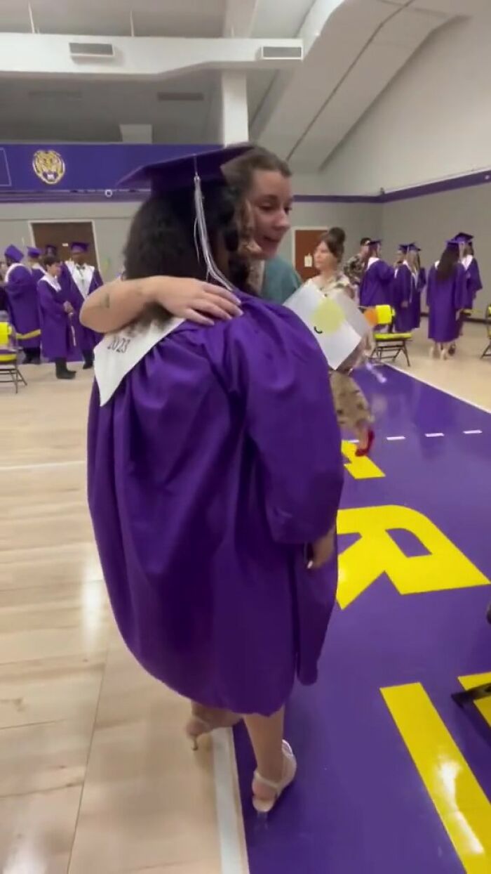 Graduating student in a purple gown receives a heartfelt hug, emphasizing meaningful teacher connections.