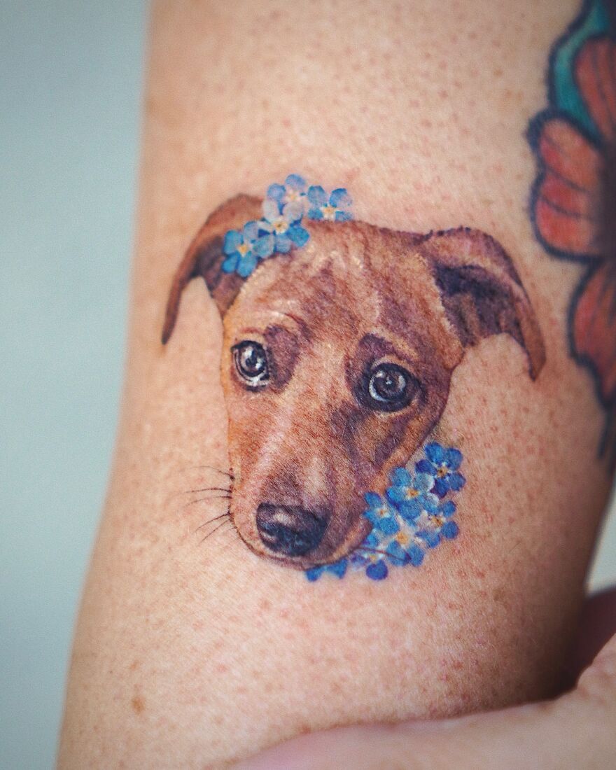 Dog tattoo with blue flowers, showcasing painting-like detail by Korean ink artist, featuring nature and animal elements.