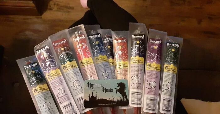 Funny products featuring mythical meat sticks with fantasy creature labels on a wooden table.