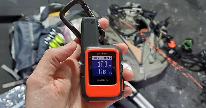 Hand holding a Garmin inReach Mini device with a bow and arrows in the background, a top Father's Day find.