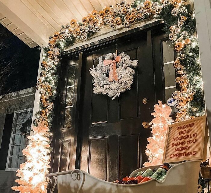 Sledge with beverages by an entrance decorated with affordable Christmas decor including lights, wreath, and ornaments.