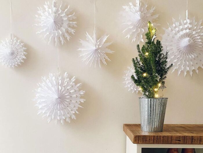 Paper snowflakes hanging on a wall next to a small lit Christmas tree, showcasing affordable Christmas decor ideas.