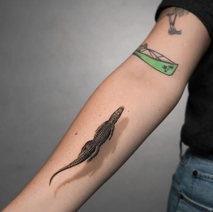 3D tattoo of a realistic crocodile on a person's forearm, showcasing detailed shadow work and texture.