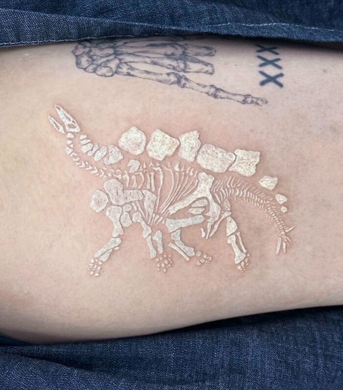 White ink dinosaur tattoo on skin, showing skeletal design in detail.