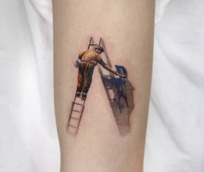 Close-up of a 3D tattoo on an arm depicting a painter on a ladder creating an optical illusion with shadow effects.