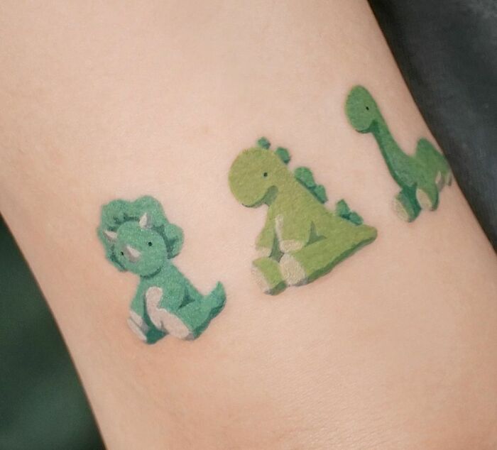 Three small, green dinosaur tattoos on skin, each with a cute and playful design.