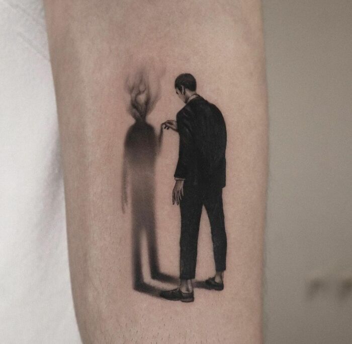 3D tattoo of a man pointing at a shadowy silhouette on arm, creating a surreal visual effect.