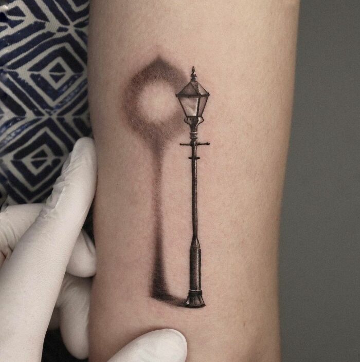 3D tattoo of a street lamp with its shadow, showcasing intricate detail and depth on forearm.