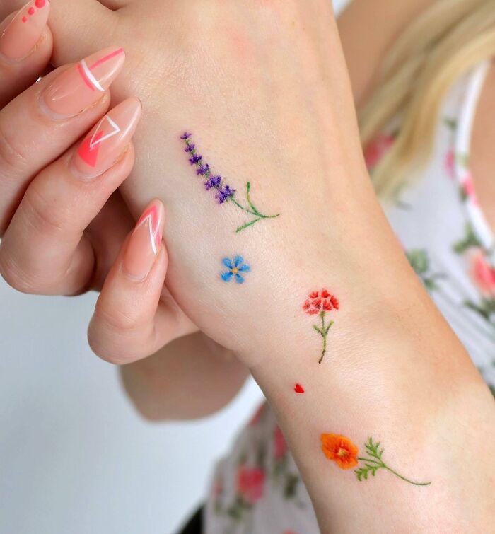 Small hand tattoos featuring colorful floral designs on a woman's hand.
