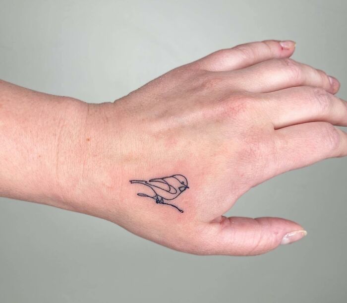 Small hand tattoo of a bird outlined on the back of a hand, highlighting minimalist design.