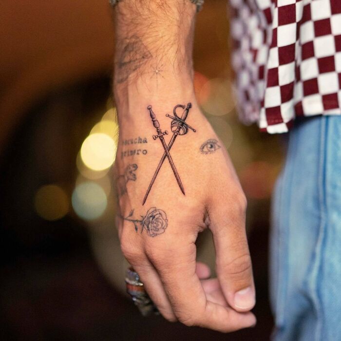 Stylish small hand tattoos featuring crossed swords, an eye, text, and a rose design, offering unique tattoo inspiration.