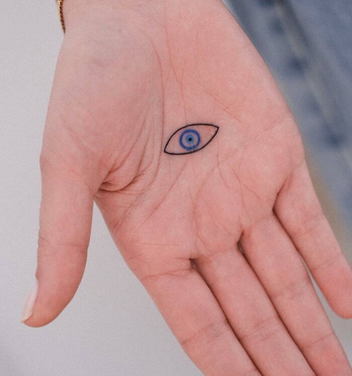 Small hand tattoo featuring a blue eye design, centered on an open palm.