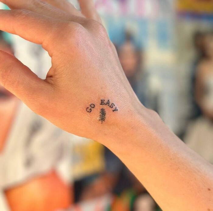 Small hand tattoo reading "Go Easy" with a tiny tree between the words.