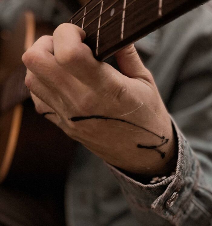 Close-up of a small hand tattoo on a wrist while playing guitar.