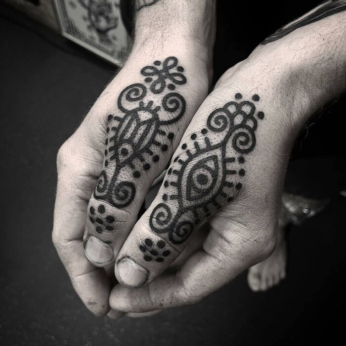 Small hand tattoos with intricate black patterns on both hands.