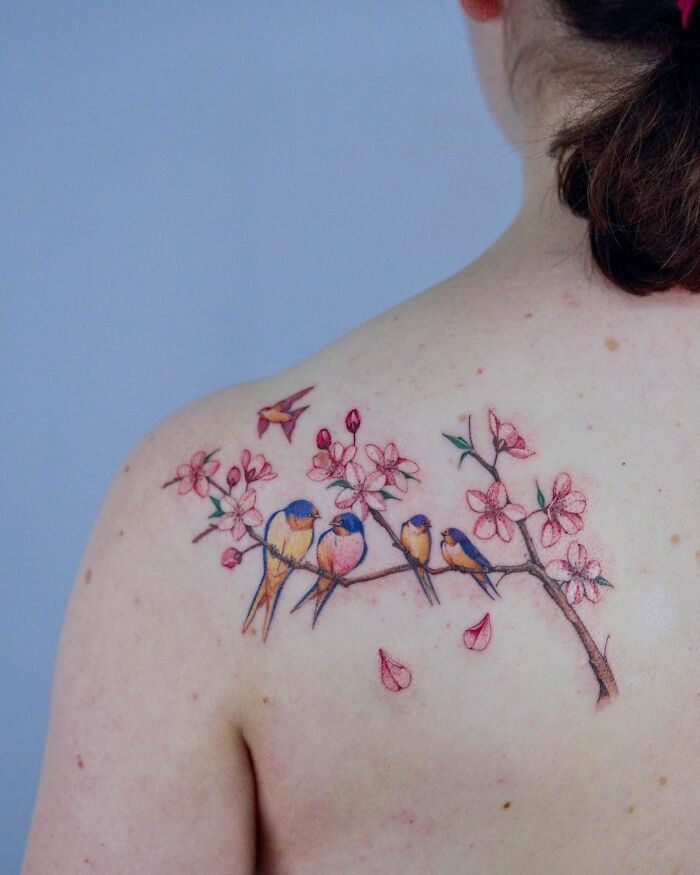 Flower tattoo with colorful birds on a shoulder, featuring delicate blossoms and petals.