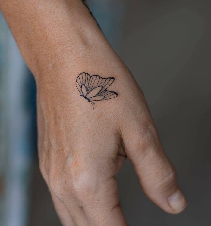 Small hand tattoo featuring a delicate butterfly design on the back of the hand.
