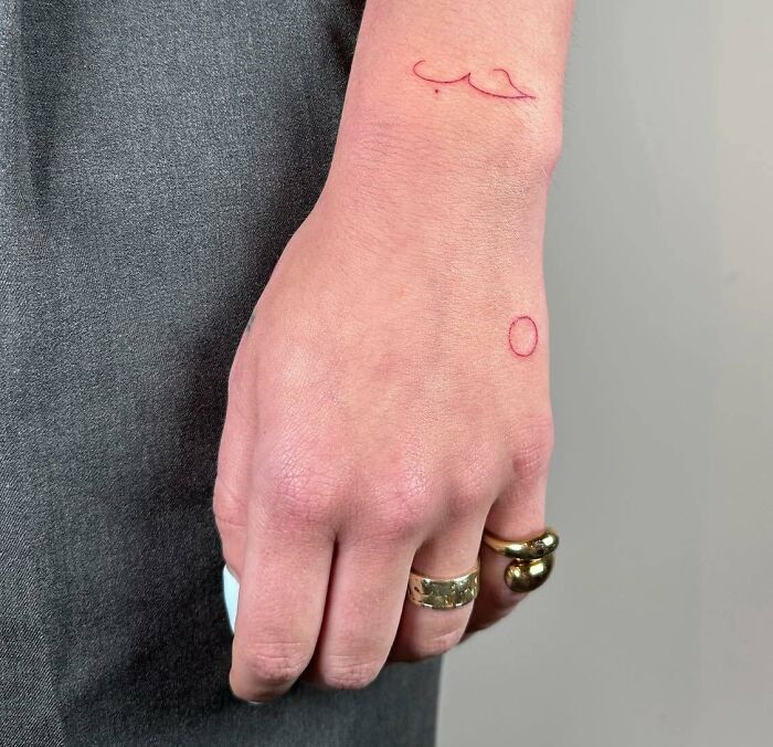 Minimalist small hand tattoos with wave and circle designs on a wrist.
