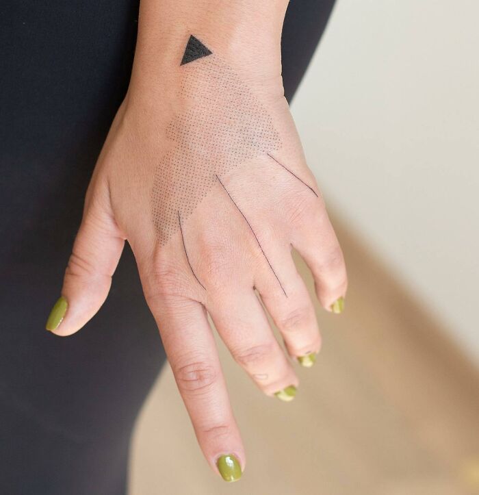 Small hand tattoo featuring geometric design on the back of a hand with green nail polish.