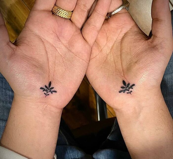 Small hand tattoos featuring matching leaf designs on open palms.