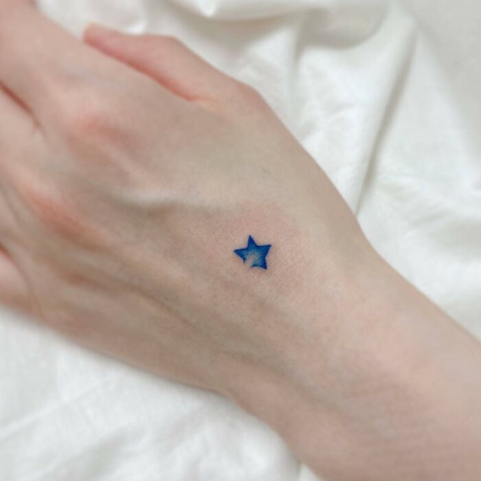 Small hand tattoo featuring a blue star on the back of a hand.