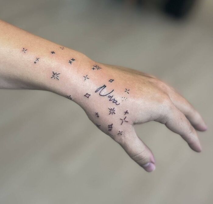 Small hand tattoo with stars and the name "Nora" on the wrist and hand.